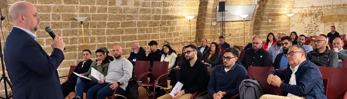 Un relatore di Snasto al microfono davanti alla platea seduta, in una sala con le pareti in pietra