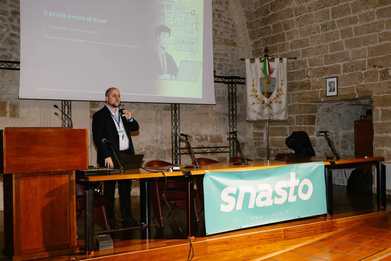 Un relatore del Marketing Lab al microfono, davanti allo schermo e al banner Snasto nella sala del Castello